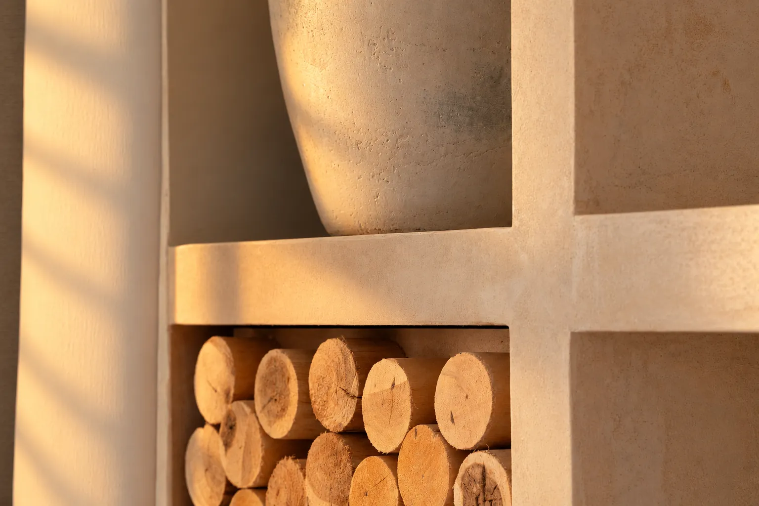 Plaster shelving with a stone vase and a log store in warm evening light