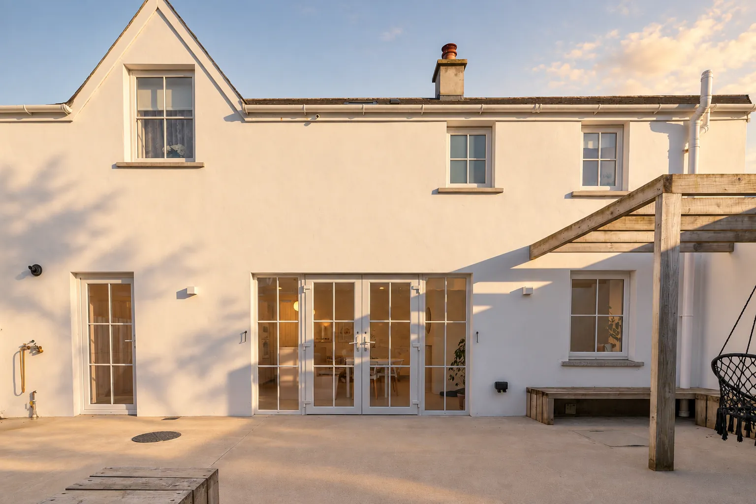 White rendered cottage rear elevation with French doors and pergola in evening sun, North Coast