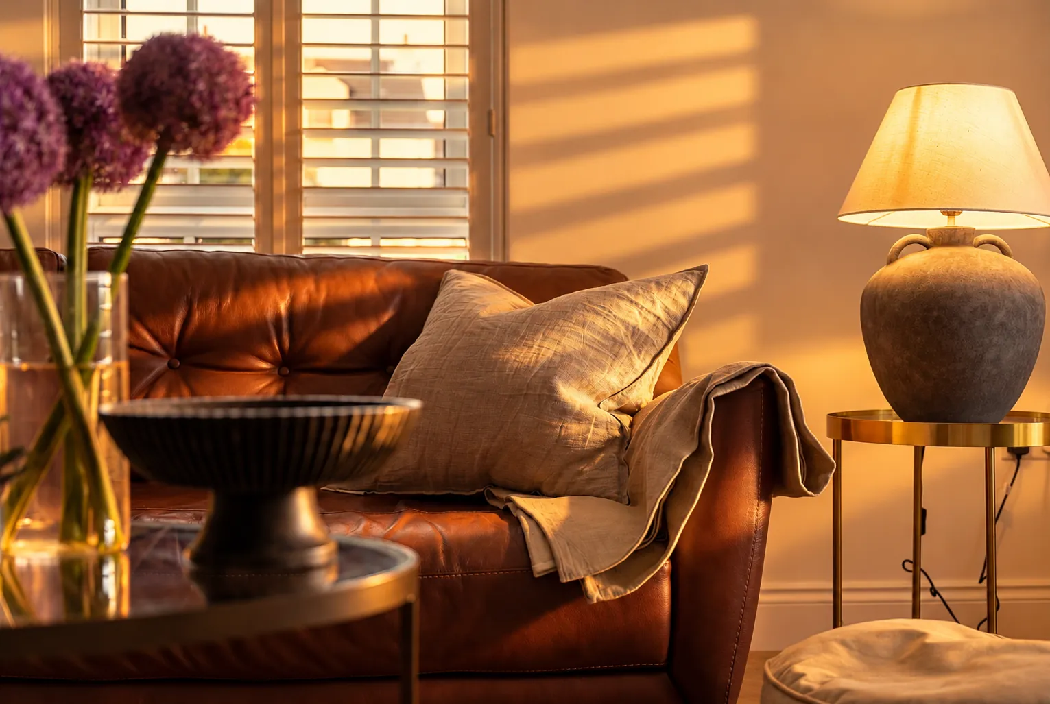 Tan leather sofa, linen cushion and stone lamp in raking golden-hour light, Bushmills