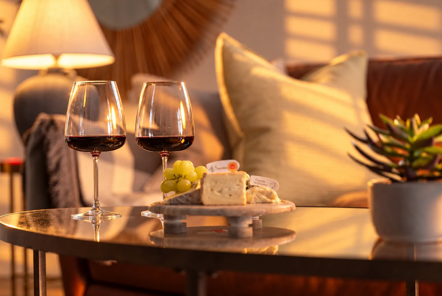 Two glasses of red wine and a cheese board on a coffee table in a Bushmills living room, warm evening light