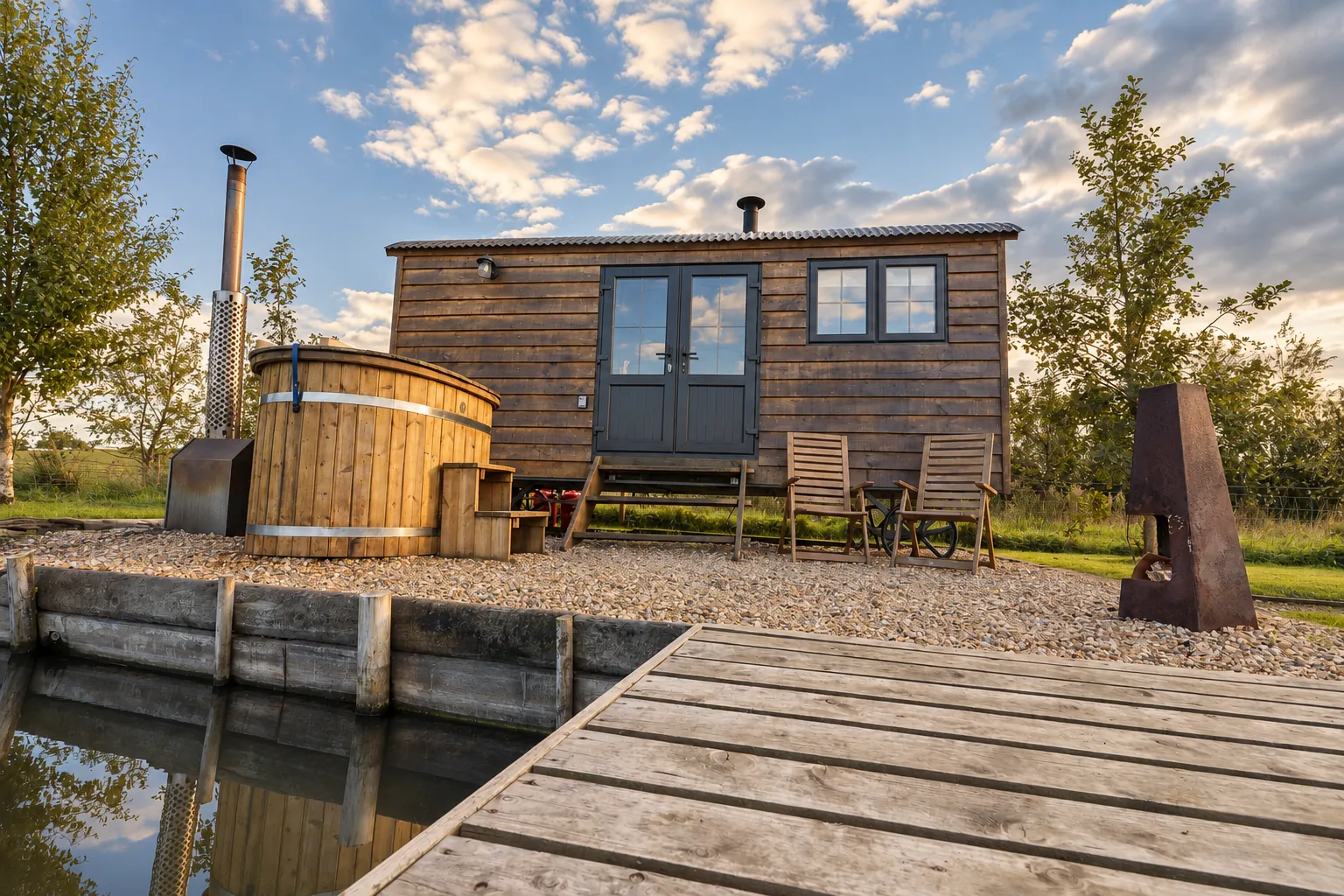 Timber shepherd’s hut with hot tub and jetty on a private lake in evening sun, Northern Ireland