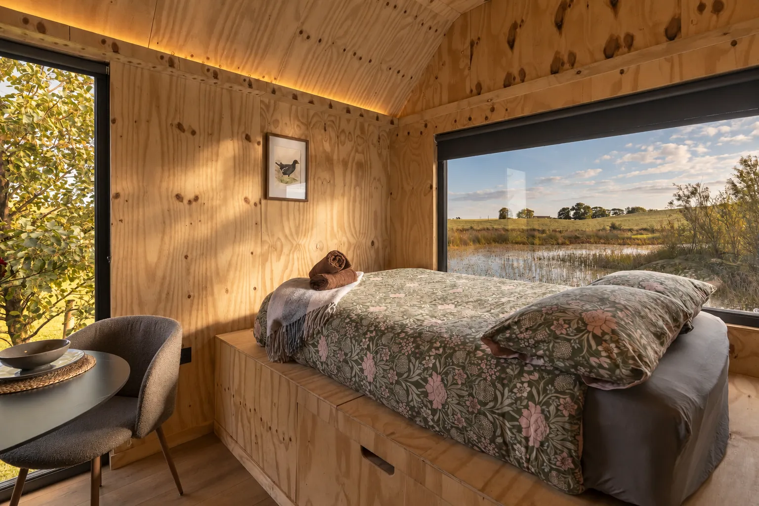 Plywood cabin bedroom with a picture window over the lake, afternoon light
